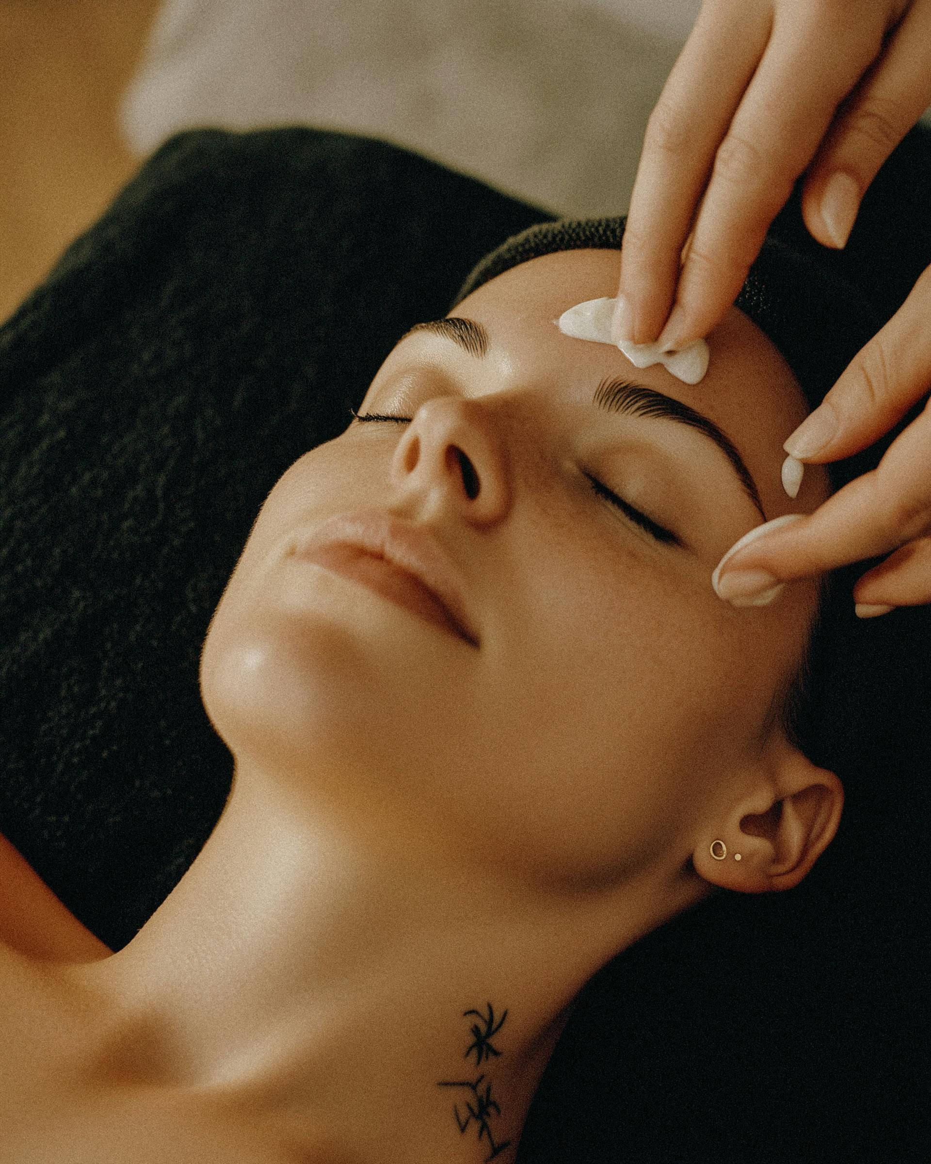 A woman with a tattoo on her neck is getting a facial massage