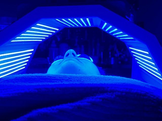 A woman is getting a blue light treatment on her face.