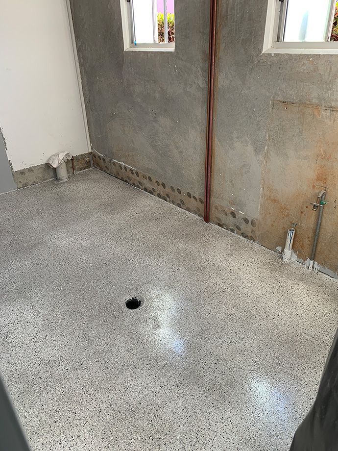 Empty room with terrazzo floor, drain, bare concrete walls, and two windows.