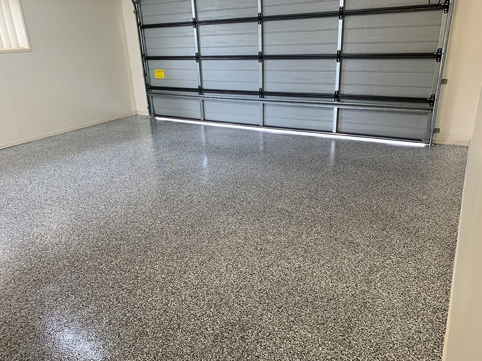 Garage with a shiny, speckled epoxy floor. A closed gray garage door is in the background.