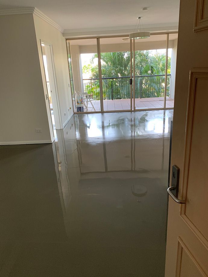 Light gray flooring reflects light from open glass doors leading to a balcony with green foliage.