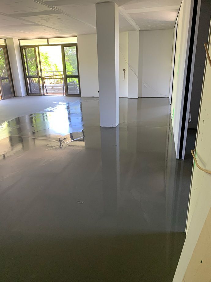 Gray, reflective floor in an empty room, white walls, large windows letting in light.