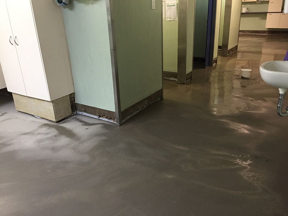 Wet, gray flooring in a room with white cabinets and a sink.