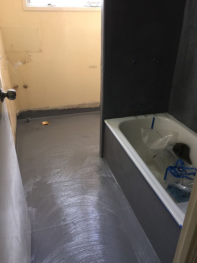 Bathroom with gray painted walls and floor; white bathtub is visible on the right.