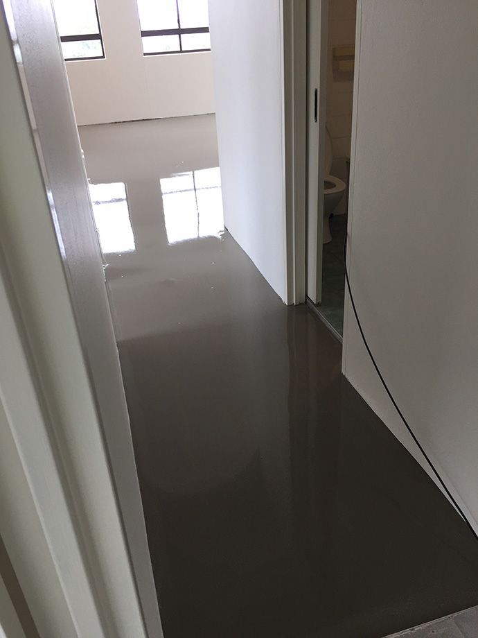 Hallway with gray, glossy floor, white walls, and a door leading to a bathroom.