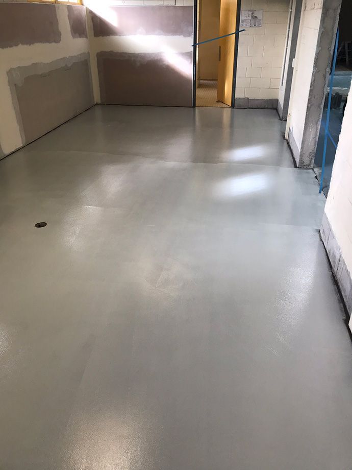 Newly poured, light gray epoxy floor in a room with unfinished walls.