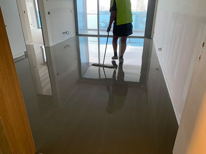 Person mopping a gray, glossy floor in a room with large windows, wearing a reflective vest.