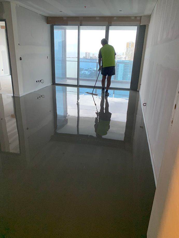 Person with squeegee cleaning a room with a shiny gray floor and a large window with a city view.