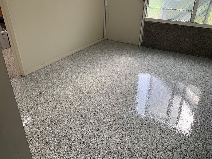 Room with a speckled, shiny floor. White and gray flecks create a textured surface. Sunlight reflects off the floor.