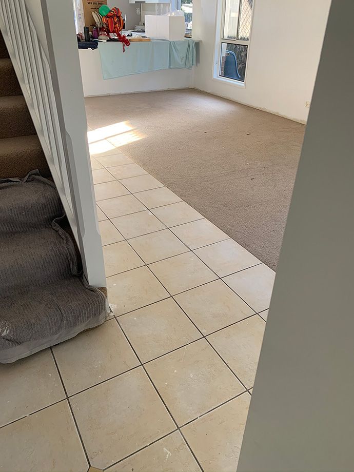 Entryway with tiled floor, leading to carpeted living area and stairs with a banister.