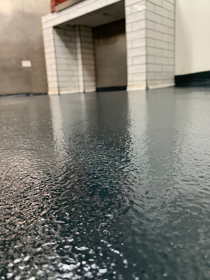 Dark, shiny floor with a textured appearance, reflecting the bottom of a white tiled fireplace.
