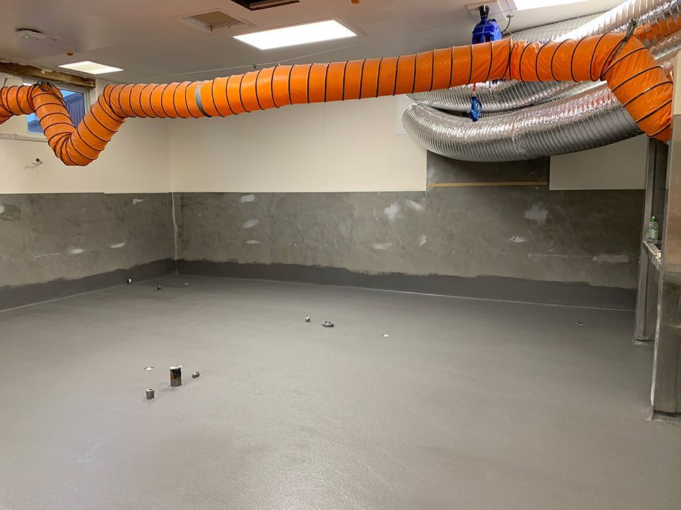 Empty room with grey floor, light walls, orange and silver ventilation ducts.
