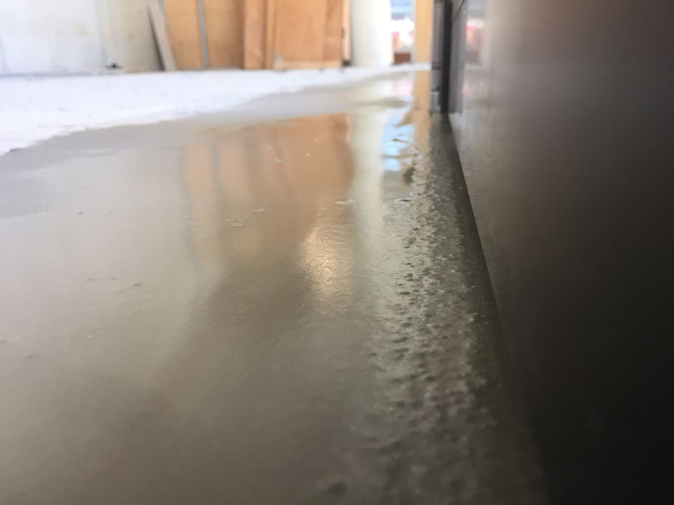 Close-up of a light-colored, wet concrete floor with an adjacent wall.