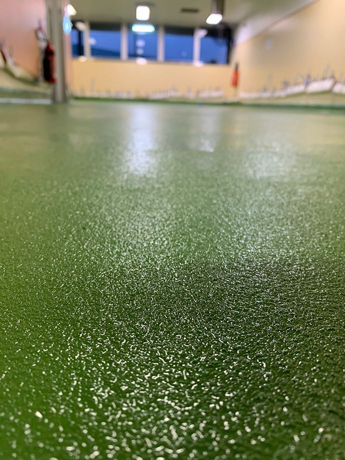 Green, textured epoxy floor. In the background, there's a light-colored wall with windows and a fire extinguisher.