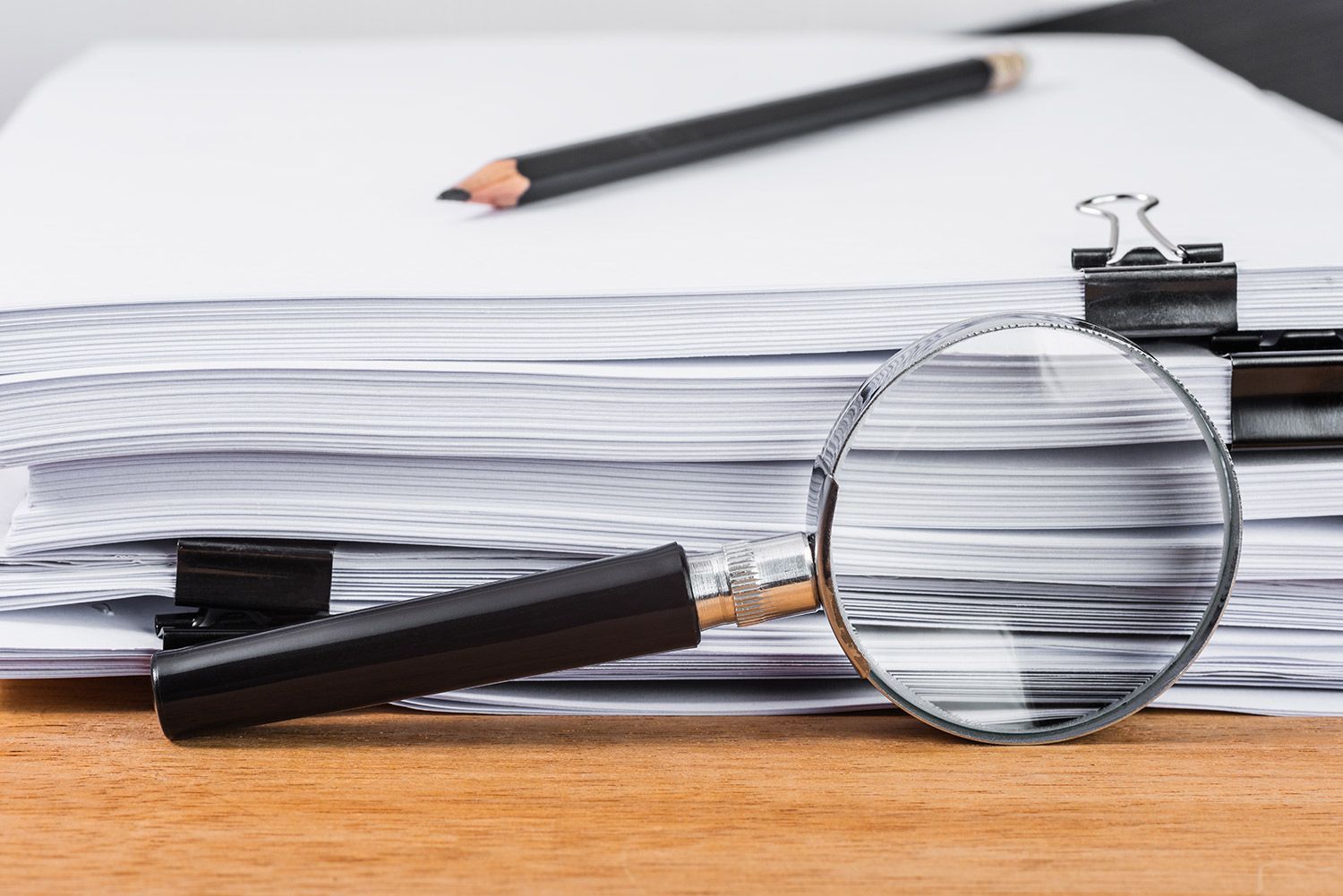 A magnifying glass rests on a stack of white papers