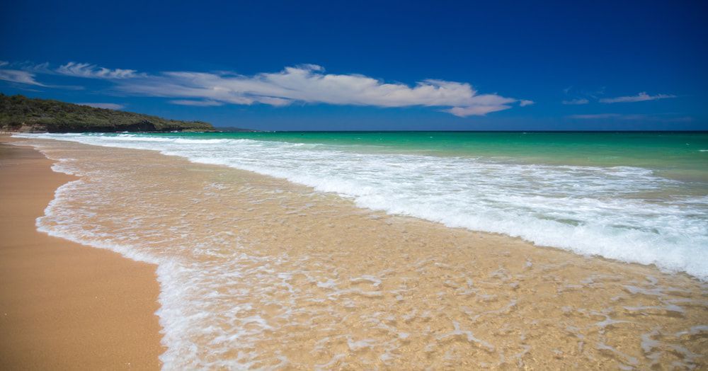 A Beach with Waves Crashing Against the Sand on A Sunny Day — BVN Landscape and Concrete Supplies in Sussex Inlet, NSW