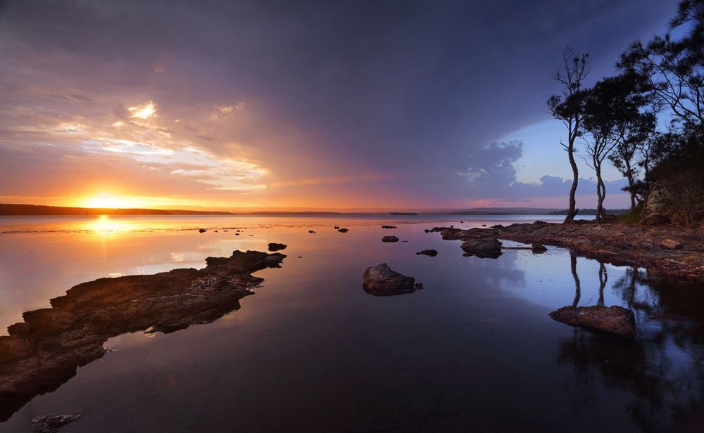 A Sunset Over a Body of Water with Rocks — BVN Landscape and Concrete Supplies in St Georges Basin, NSW