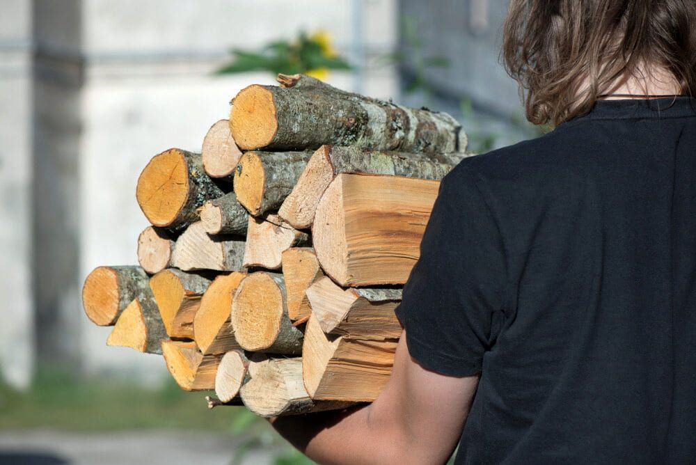 Person Carrying a Stack of Cut Logs Outdoors — BVN Landscape and Concrete Supplies in St Georges Basin, NSW