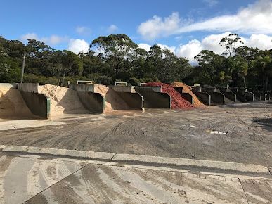 A Row of Dumpsters Are Lined up In a Dirt Field with Trees — BVN Landscape and Concrete Supplies in Nowra, NSW