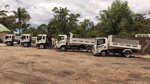 A Row of Dump Trucks Are Parked in A Dirt Lot — BVN Landscape and Concrete Supplies in Nowra, NSW