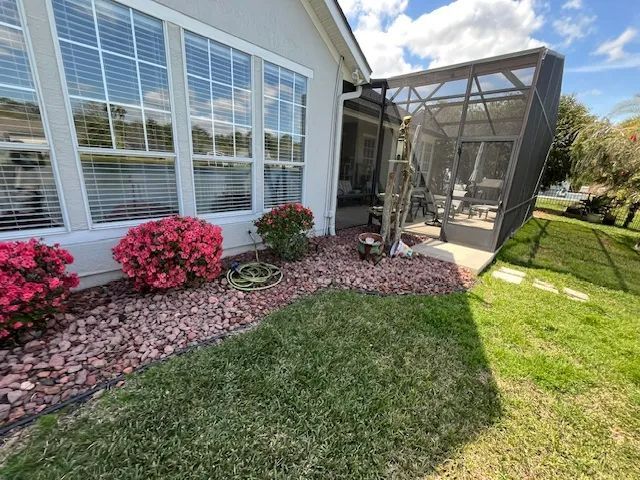 House exterior with screened patio, pink shrubs, and a grassy yard under sunny skies