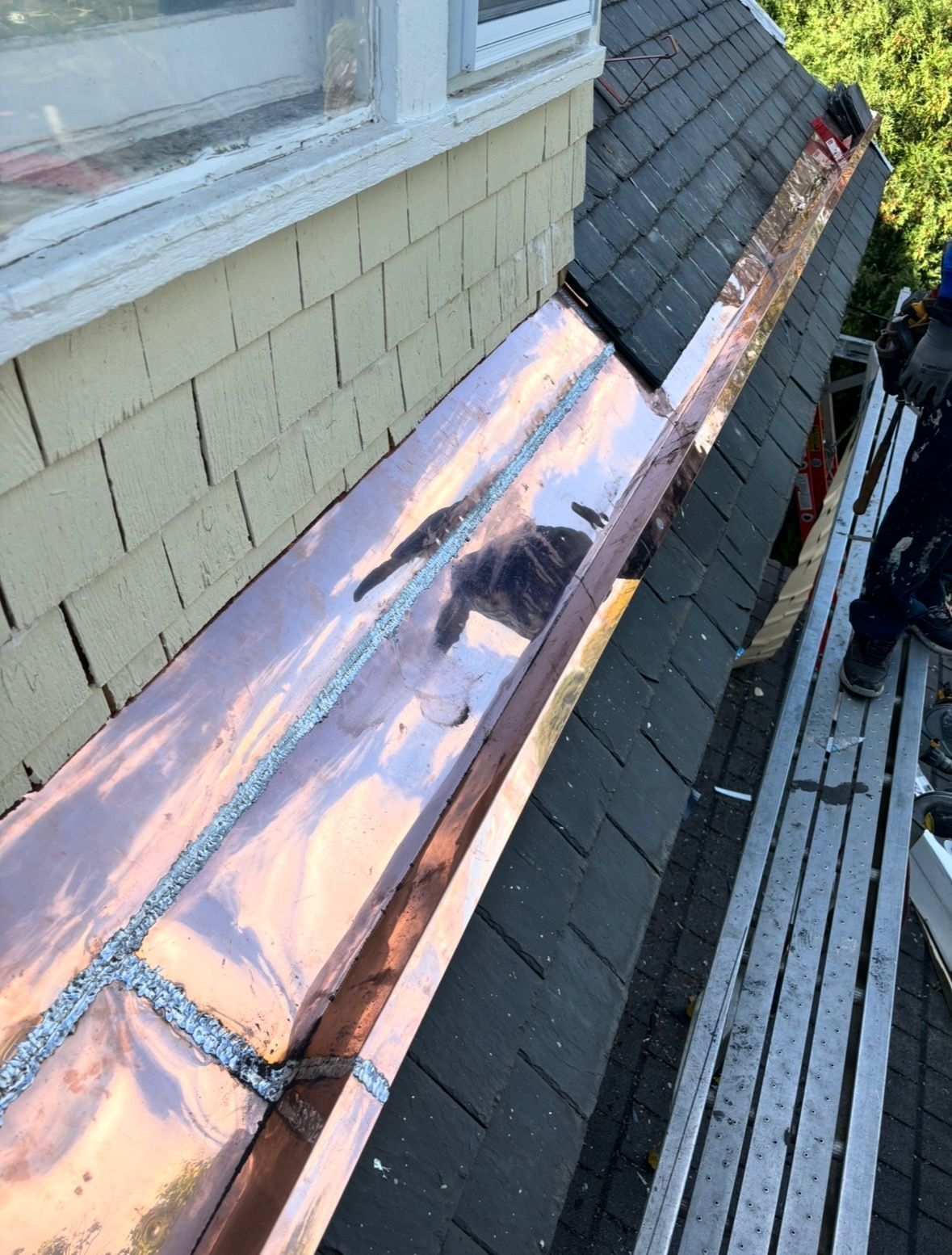 A copper gutter is being installed on the roof of a house.