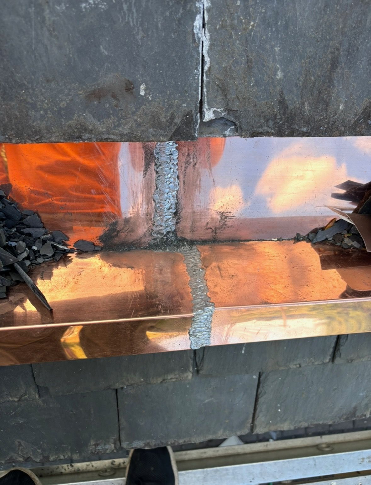 A person is working on a copper gutter on a roof.