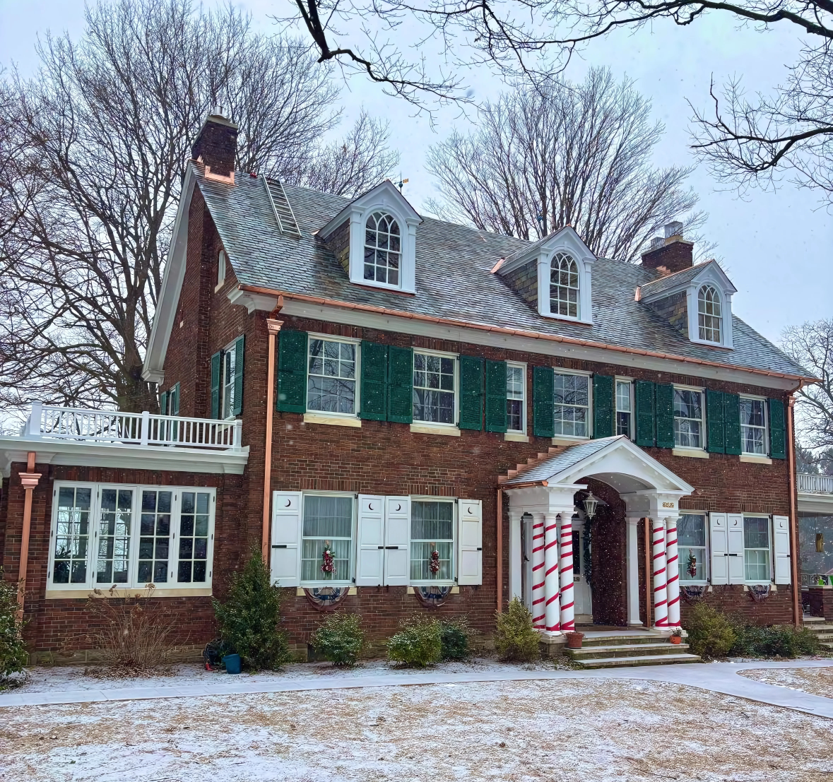 A large brick house with green shutters is covered in snow.