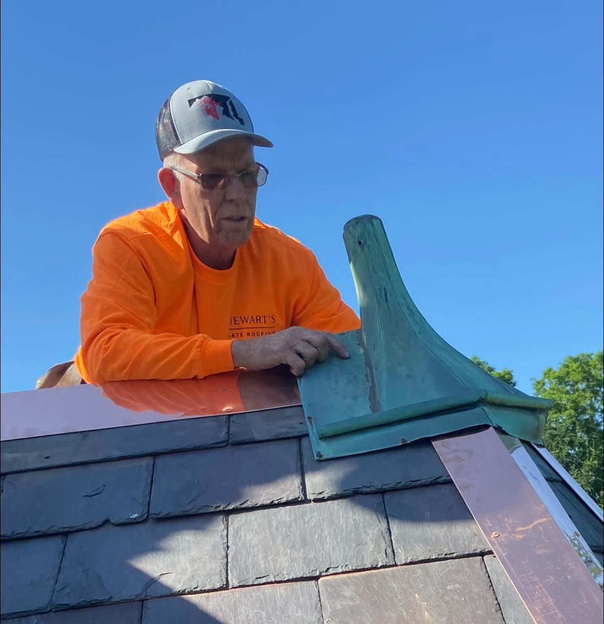 A man in an orange shirt is sitting on top of a roof