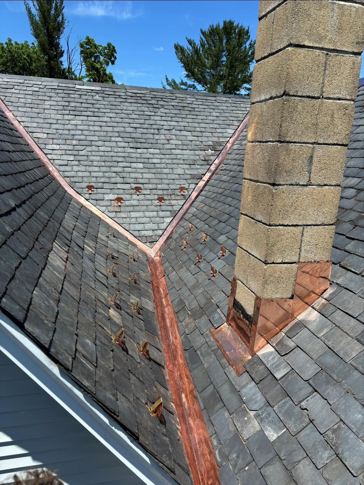 A roof with a chimney on it and a copper gutter.