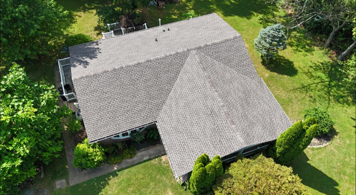 An aerial view of a house with a gray roof surrounded by trees and grass.