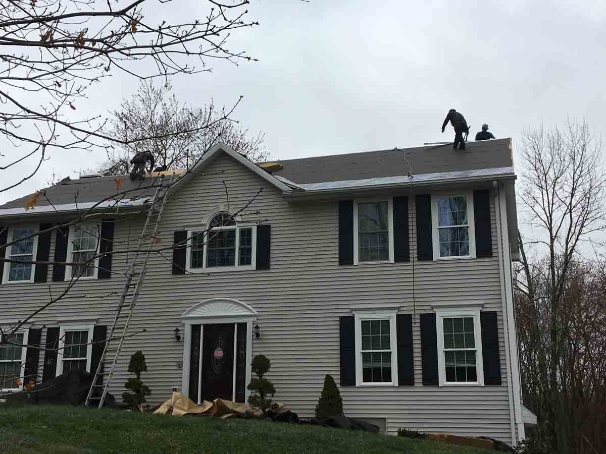Snow-covered two-story house with damaged siding and a person on the roof.