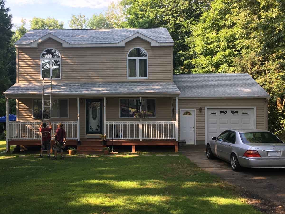 Two-story beige house with front porch, garage, and parked silver car in a grassy yard