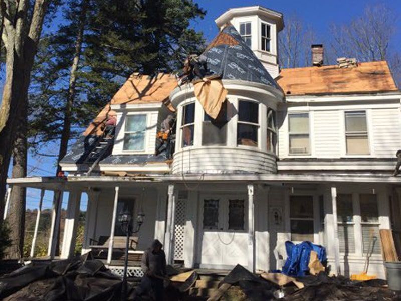 Damaged two-story house with fire damage, boarded windows, and a porch under repair