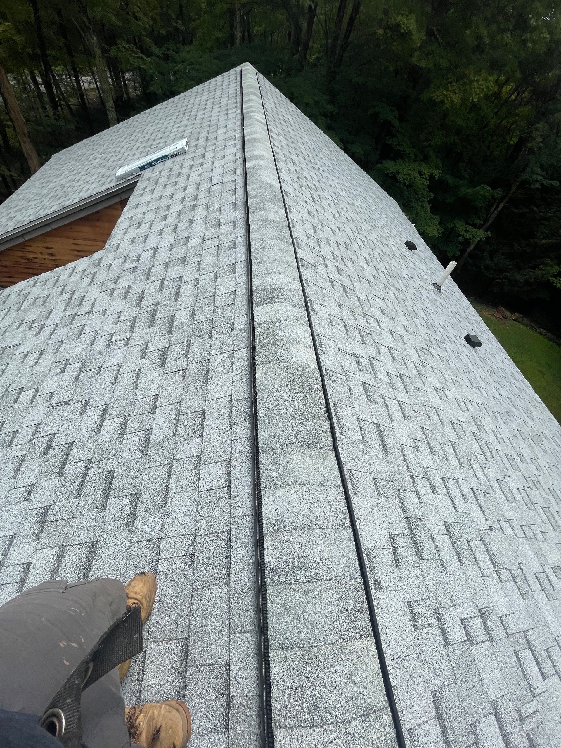 Roofing shingles being installed on a steep, gray roof with trees in the background