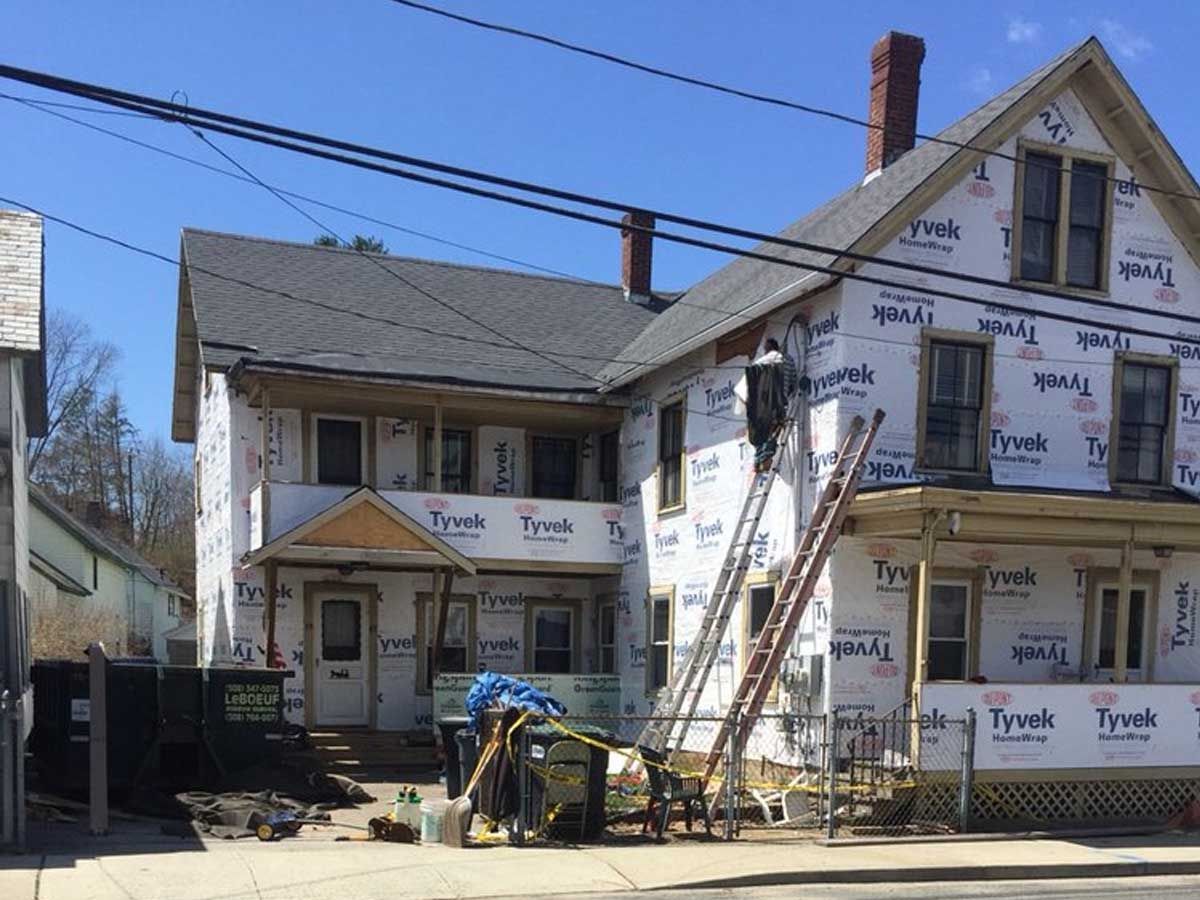 House under construction with ladders, scaffolding, and exposed insulation beside a small home.