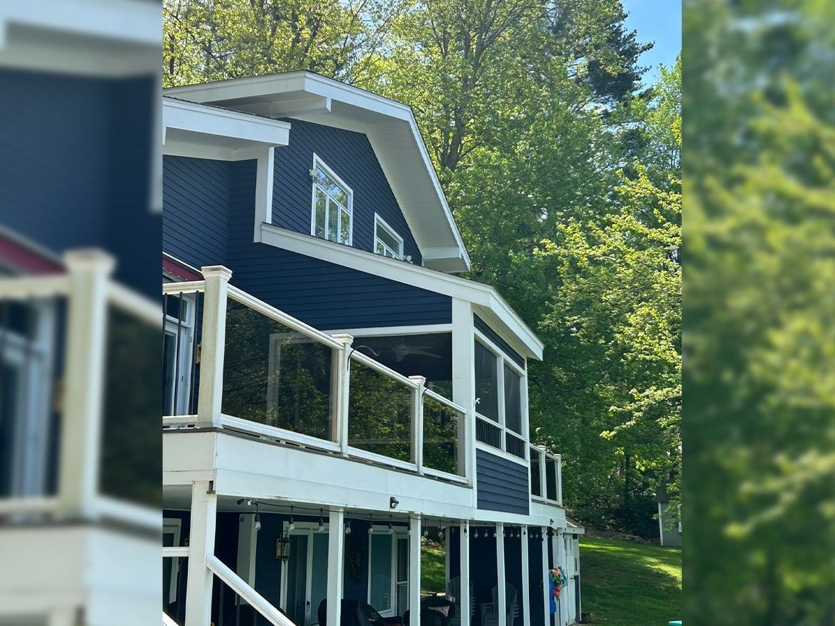 Blue house with white balconies and trim surrounded by green trees on a sunny day