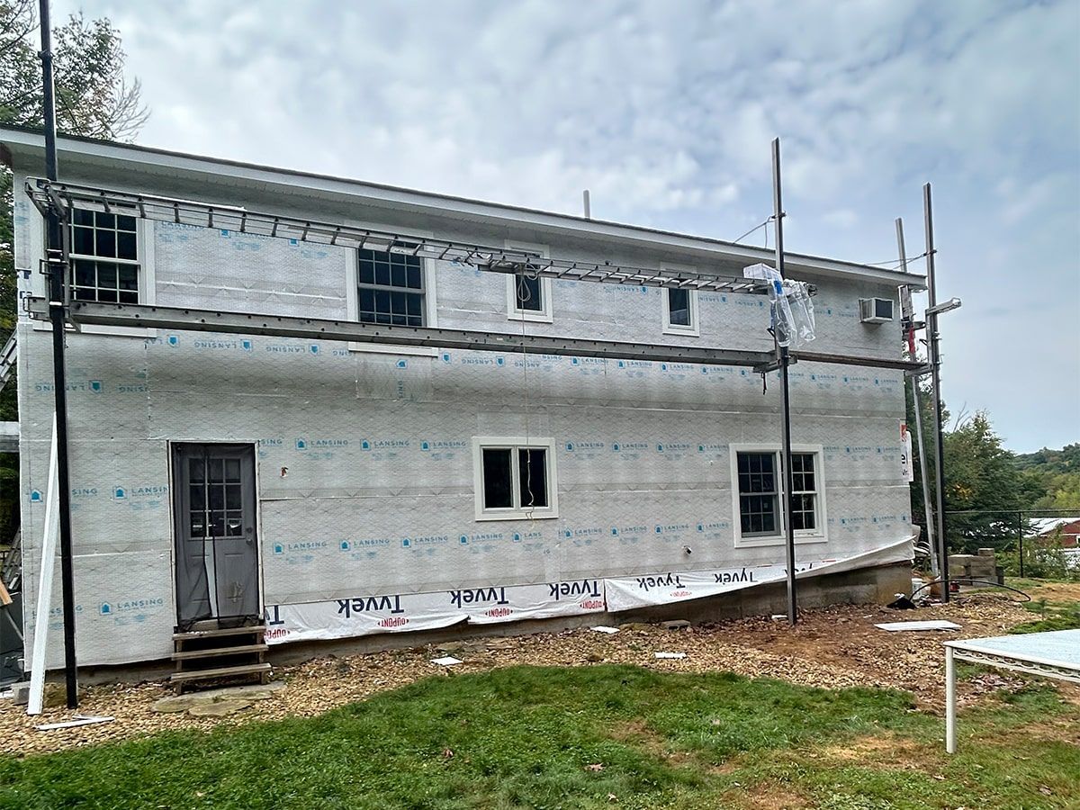 Partially finished two-story gray house with scaffolding under a cloudy sky