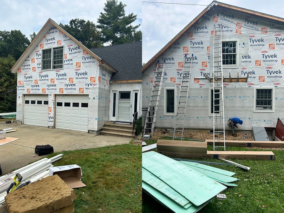 Partially built house wrapped in Tyvek, with unfinished garage and green siding panels in the yard