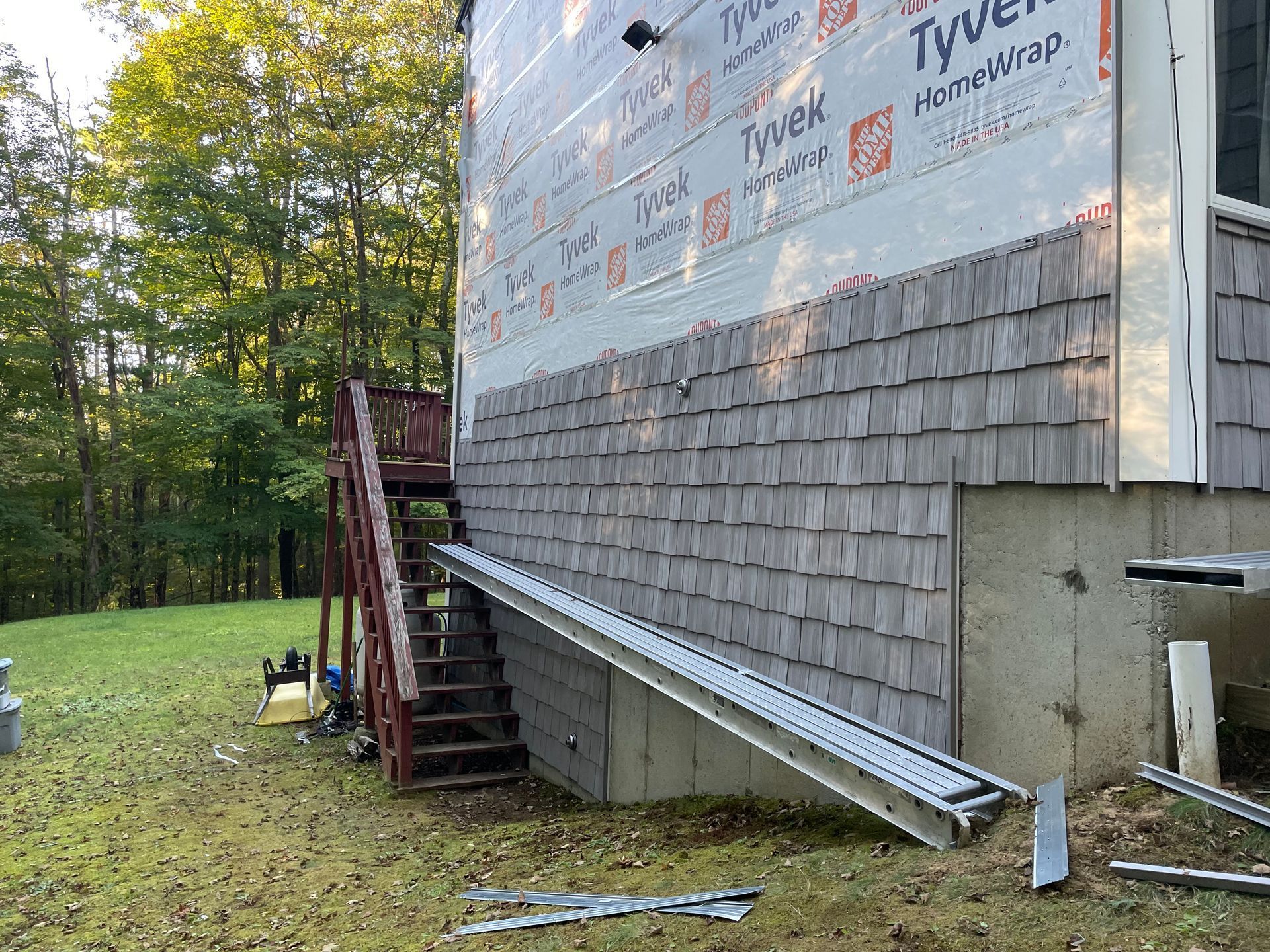Partially sided house with stairs and scaffolding in a wooded yard