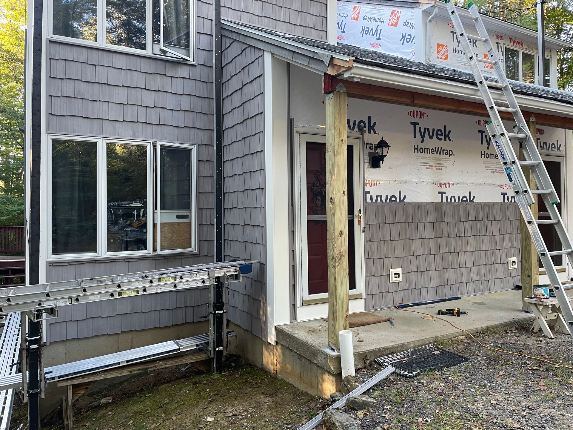 Partially finished house exterior with gray siding, windows, scaffolding, and a ladder by the entryway