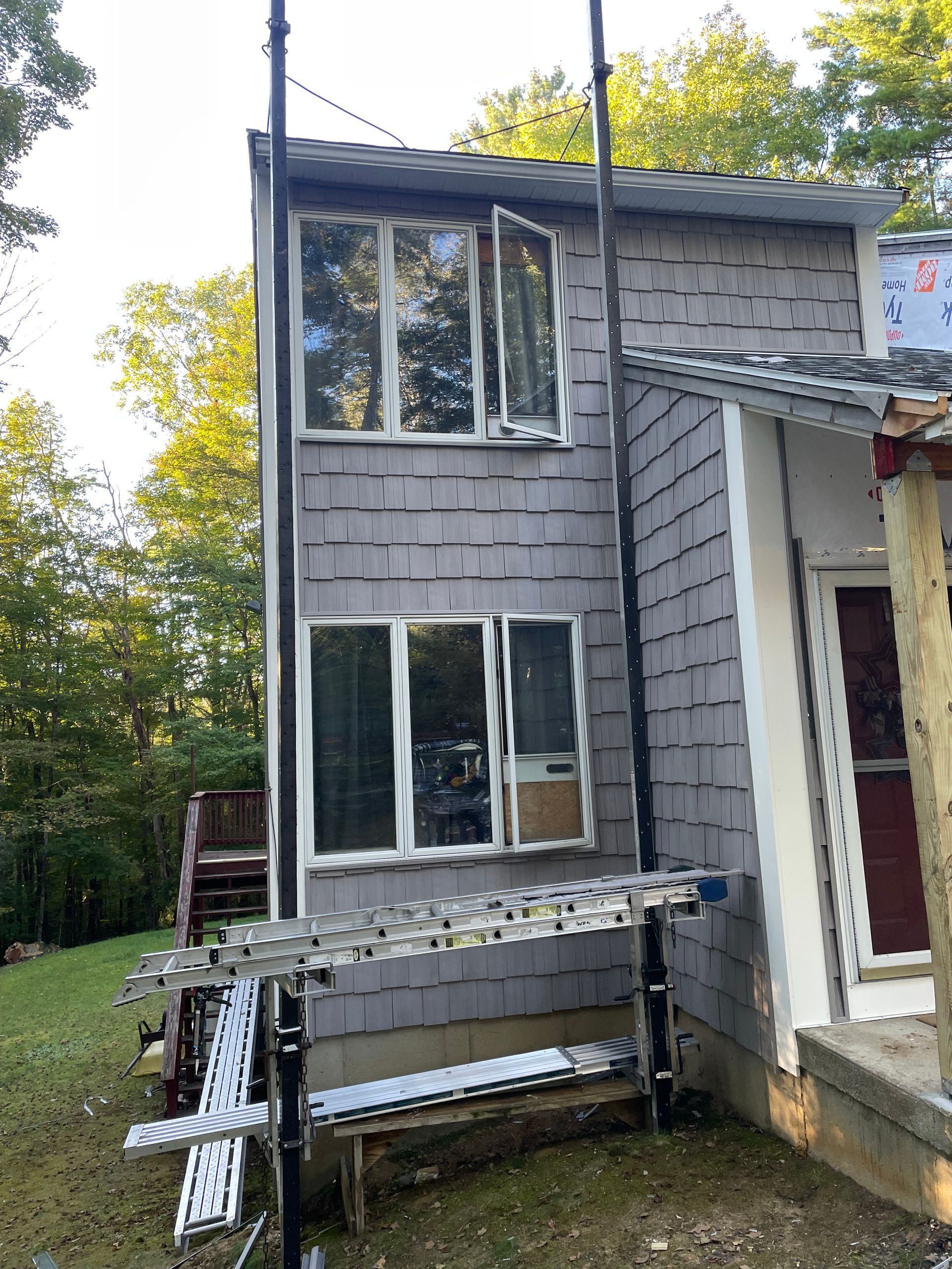 Gray-sided house with large windows and a metal ramp on the left side, surrounded by trees.