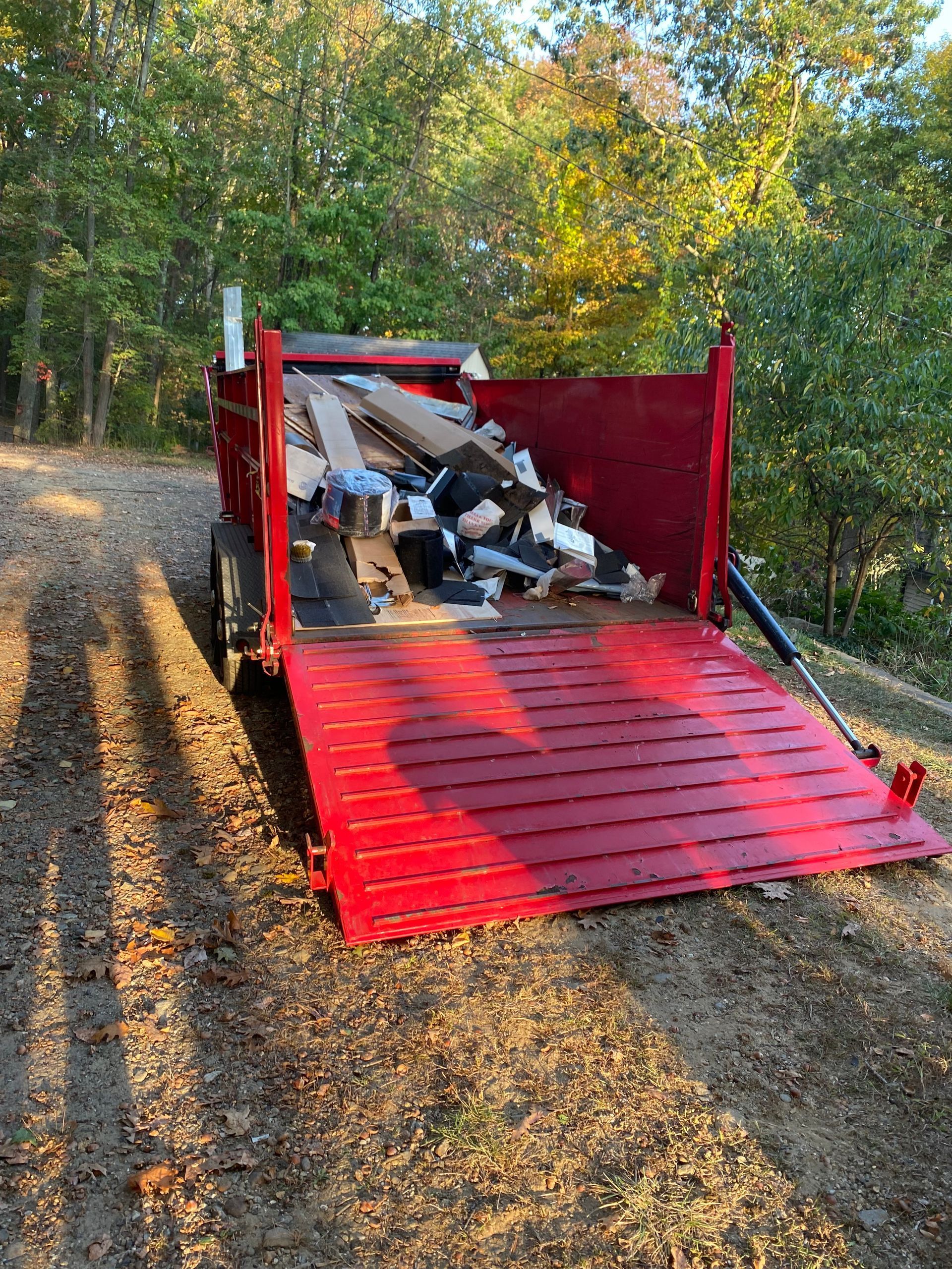 Red dump truck unloading a pile of scrap metal on a dirt road in a wooded area