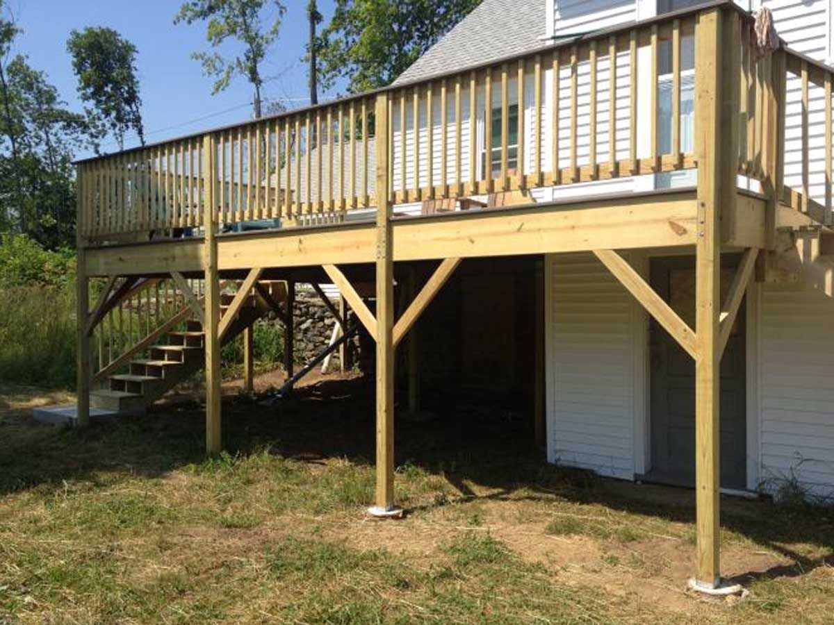 Elevated wooden deck with stairs and railings beside a house, standing over a grassy yard