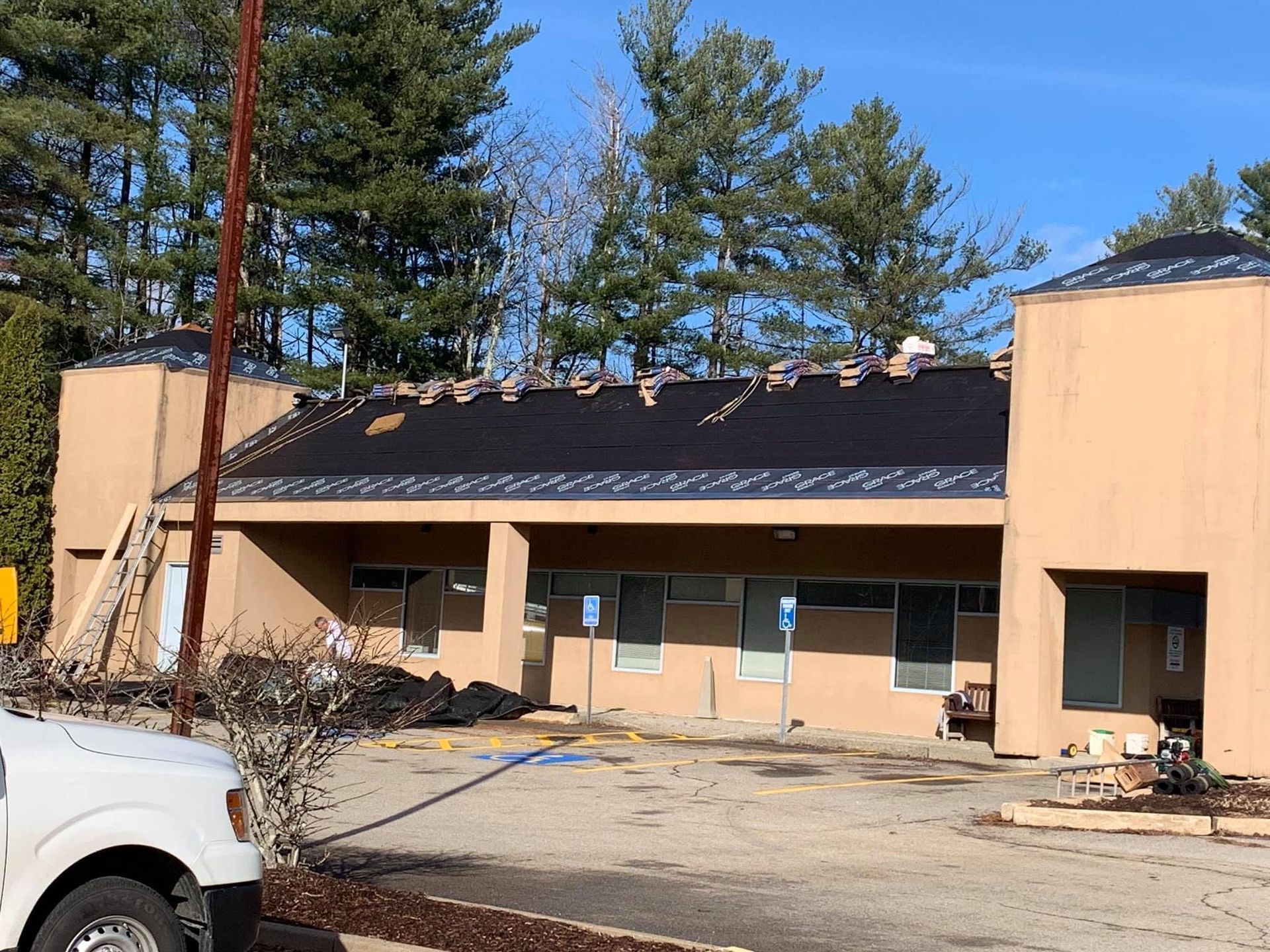 Damaged beige building with a partially collapsed roof and debris in the parking area.