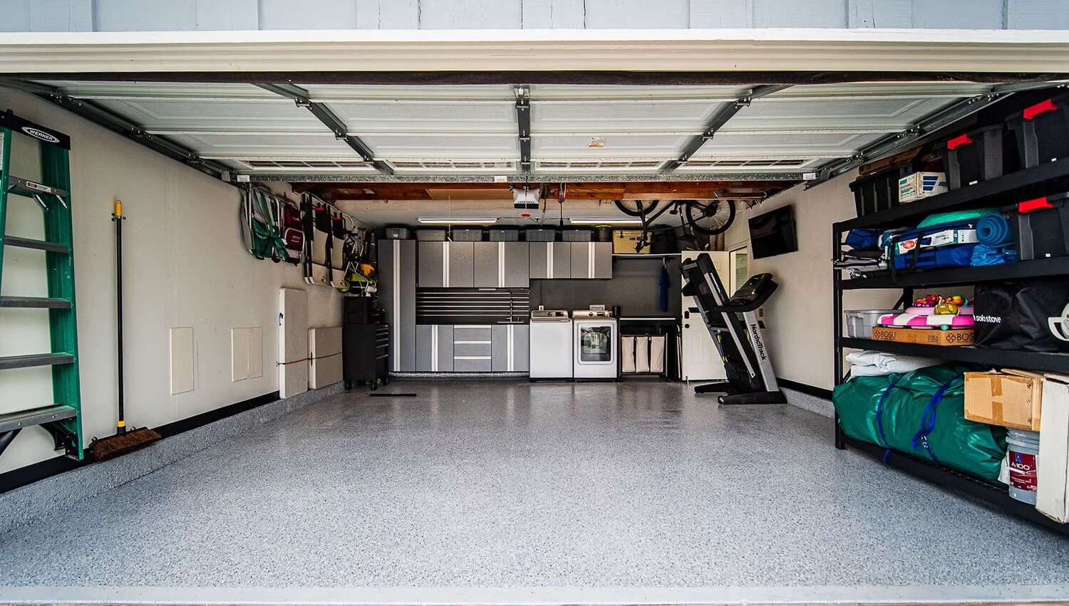 Spacious garage with open door, white cabinets, speckled floor, and organized storage shelves on the right.