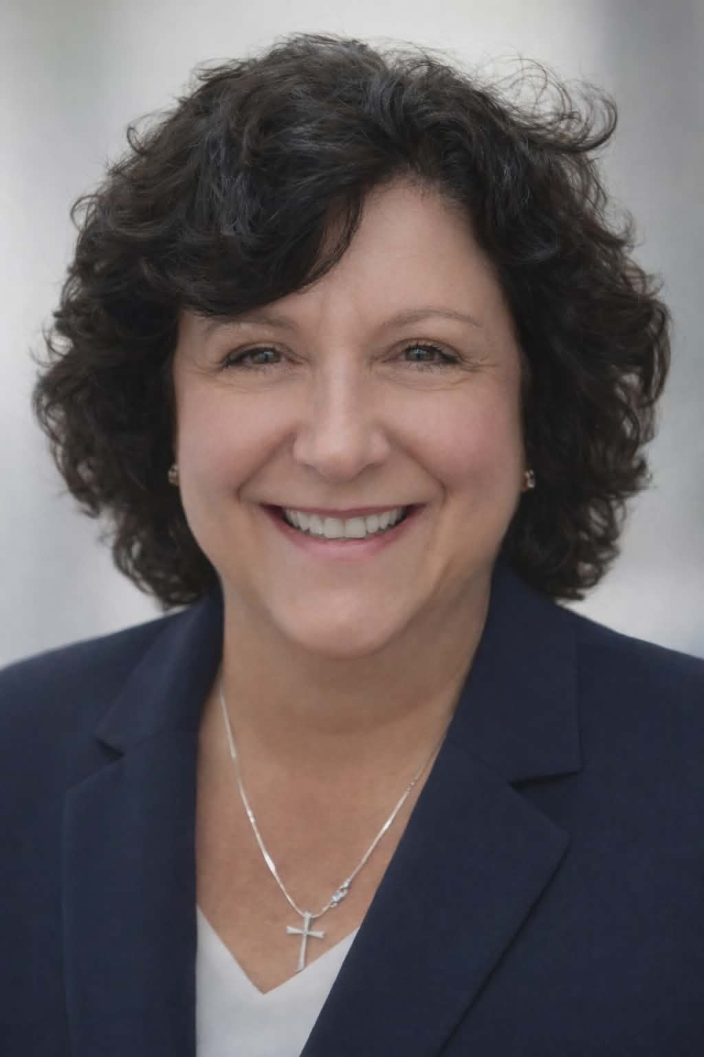 Smiling woman in navy blazer with curly dark hair on a light gray background