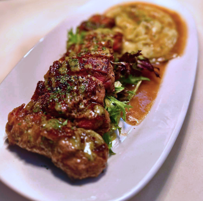 Grilled steak with green sauce, served on a bed of greens, alongside mashed potatoes and gravy.