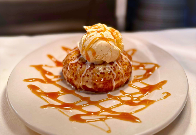 Dessert on white plate: round pastry with ice cream and caramel drizzle.
