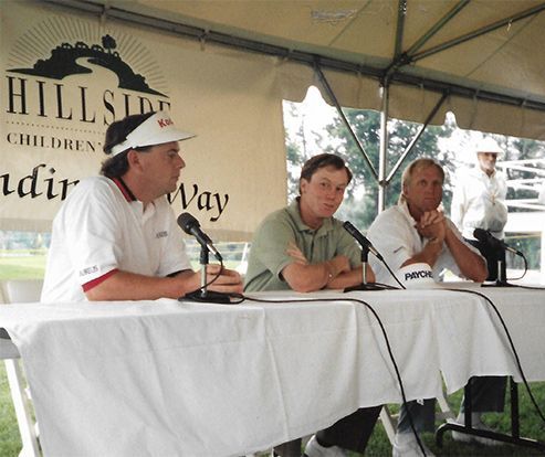 Three men sit at a table with microphones in front of a sign that says hillside